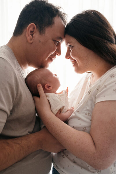 Parents face à face se touchant le front et tenant ensemble leur nouveau-né entre eux, doux contre-jour de lumière naturelle