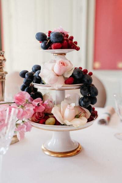 Présentoir à fruits en porcelaine dorée sur trois étages, garni de raisins noirs, framboises et roses pêche pour un mariage