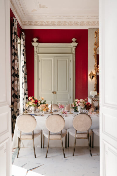 Salle aux murs rouge carmin et moulures dorées, table dressée avec fleurs roses et pêche pour un mariage en Hauts-de-Seine