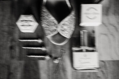 Gros plan flou artistique en noir et blanc sur les accessoires de la mariée : bague hexagonale, peigne et flacon de parfum