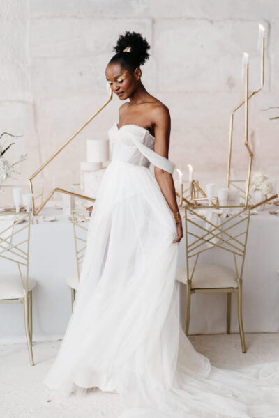 Mariée en bustier tulle blanc et maquillage doré posant devant une table minimaliste blanc et or, mariage en Hauts-de-Seine