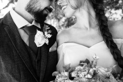 Gros plan des visages des mariés se souriant, boutonnière rose sur le veston et tresse de la mariée
