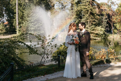 Mariés se regardant tendrement devant une fontaine avec arc-en-ciel dans un parc d'automne