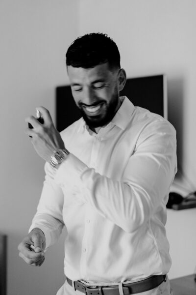 Marié en chemise blanche vaporisant du parfum avec un grand sourire lors des préparatifs