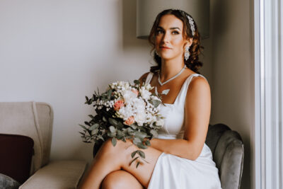 Mariée assise dans un fauteuil tenant un bouquet de roses roses et blanches avec bijoux étincelants à Clamart
