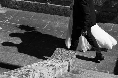 Jambes de mariés montant des marches en pierre en plein soleil, ombre portée sur le dallage