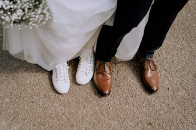 Pieds de la mariée en Converse blanches et ceux du marié en derbys marron, bouquet de gypsophile