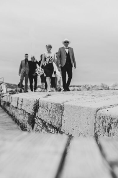 Cortège de mariage marchant sur un quai en pierre au bord de la mer, vus en contre-plongée
