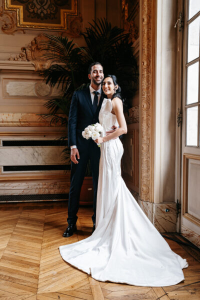 Mariés souriants dans un salon haussmannien doré à Clamart, elle en robe bustier à traîne et lui en costume noir