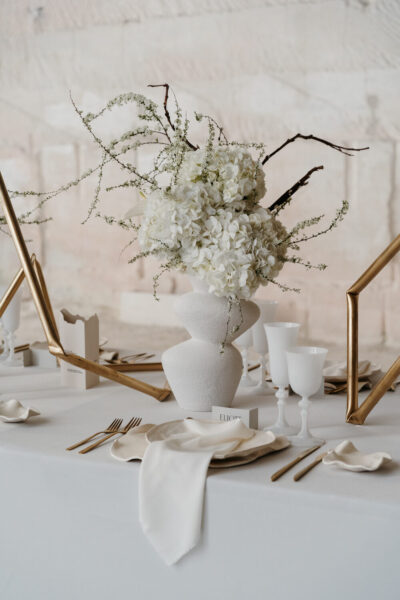 Centre de table avec vase texturé blanc et bouquet d'hortensias blancs en effusion, couverts dorés