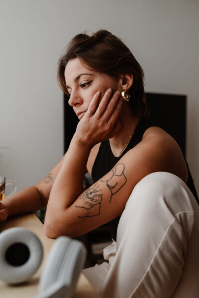 Femme tatouée appuyée sur un bureau, main posée sur la joue, regard pensif dans une ambiance lifestyle