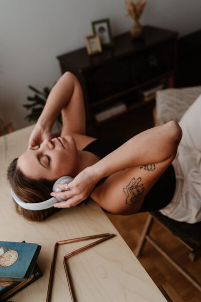 Femme tatouée allongée sur une table avec un casque audio blanc sur les oreilles, yeux fermés