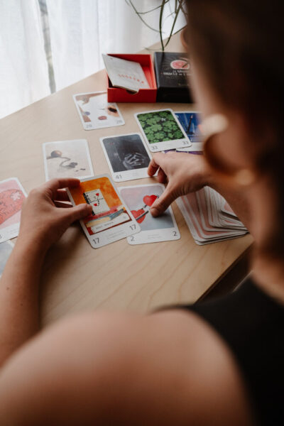 Femme étalant des cartes oracle colorées sur une table en bois clair, ambiance divinatoire et introspective