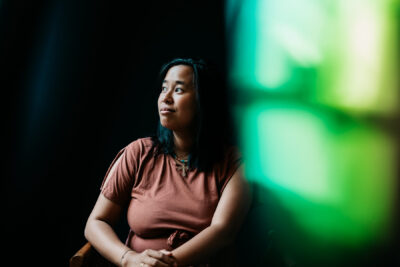 Jeune femme en t-shirt rouille levant les yeux avec un sourire espiègle, lumière verte en arrière-plan