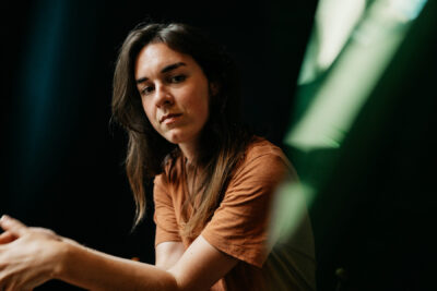 Jeune femme en t-shirt rouille regardant l'objectif avec intensité, lumière verte balayant le fond sombre