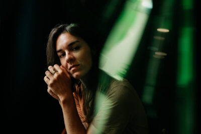 Femme brune appuyant son menton contre ses mains avec un regard doux, lumière verte colorant le fond