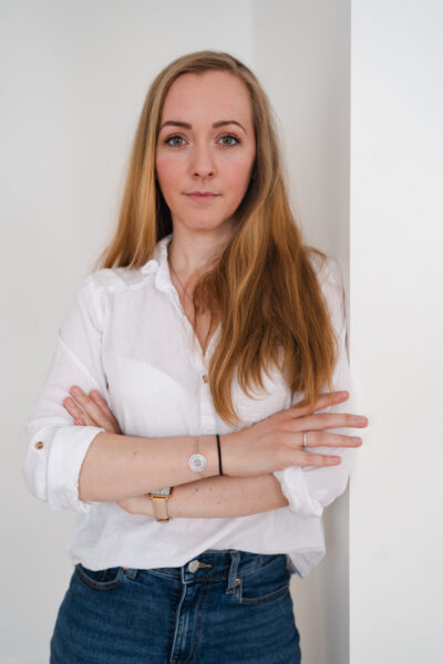 Femme en chemise blanche bras croisés regardant l'objectif avec assurance sur fond blanc épuré