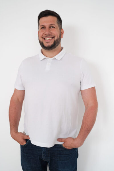Homme souriant en polo blanc sur fond blanc, mains dans les poches, ambiance décontractée